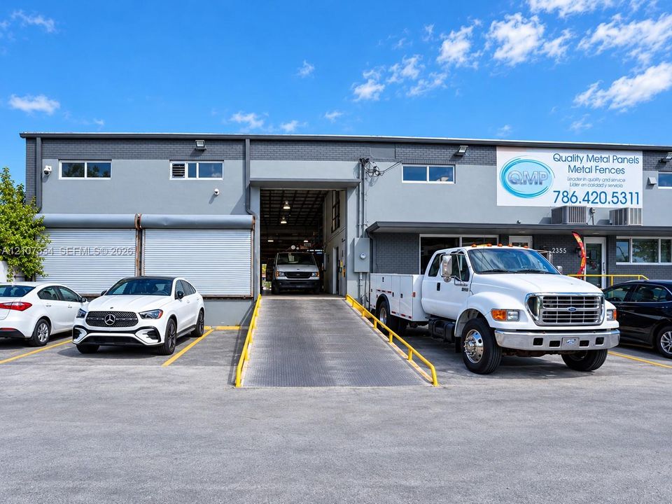 Commercial facility featuring a concrete exterior, elevated loading ramp, two roll-up service doors, and dedicated parking area