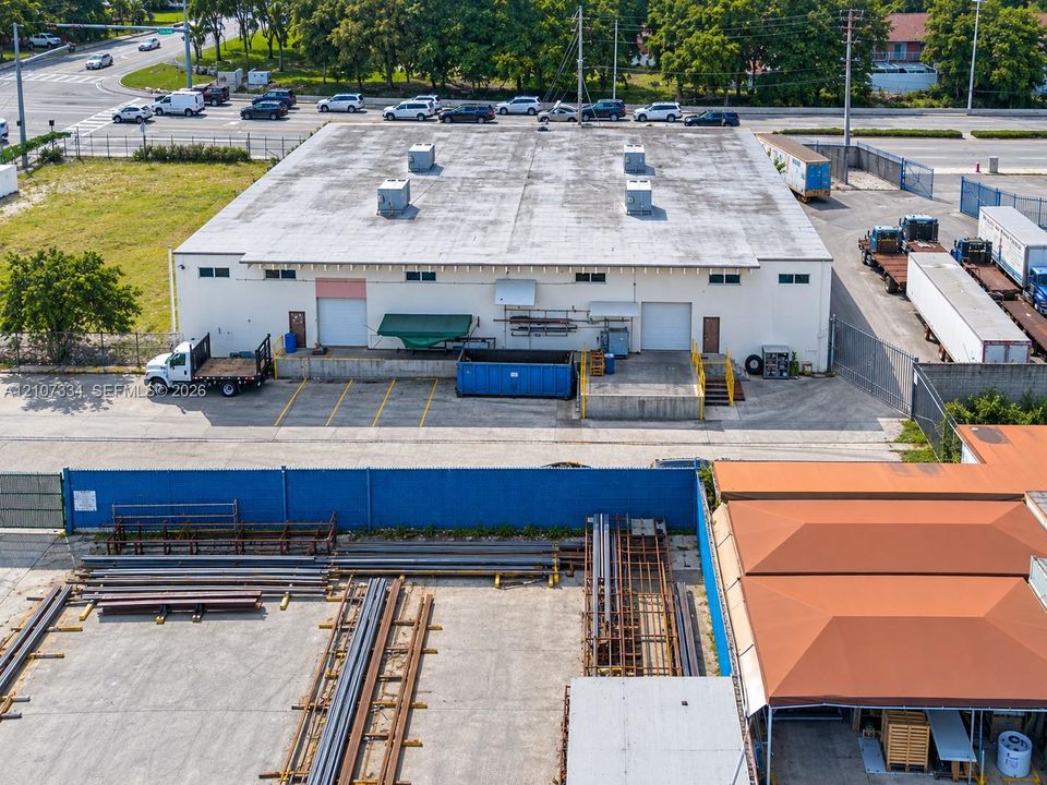 Industrial facility featuring two grade-level loading doors, a dedicated loading dock with metal stairs, paved exterior storage areas, and perimeter fencing