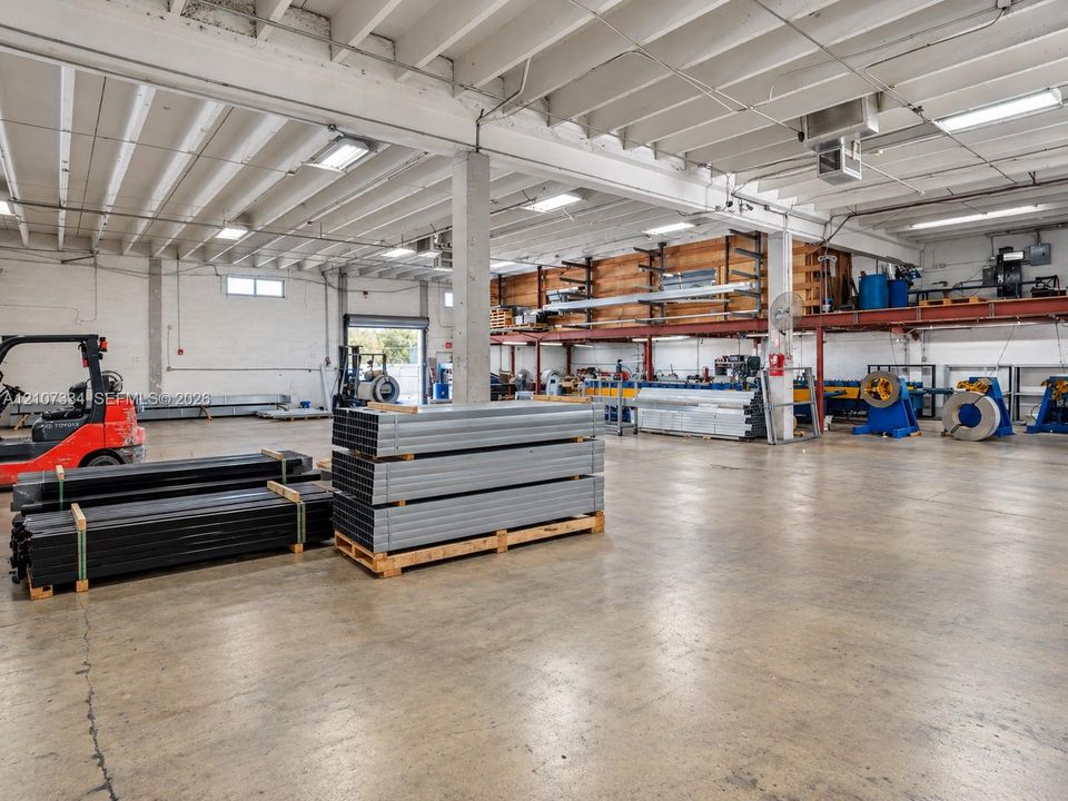 Industrial warehouse space featuring concrete flooring, exposed beam ceiling, mezzanine level storage, and high-intensity overhead lighting