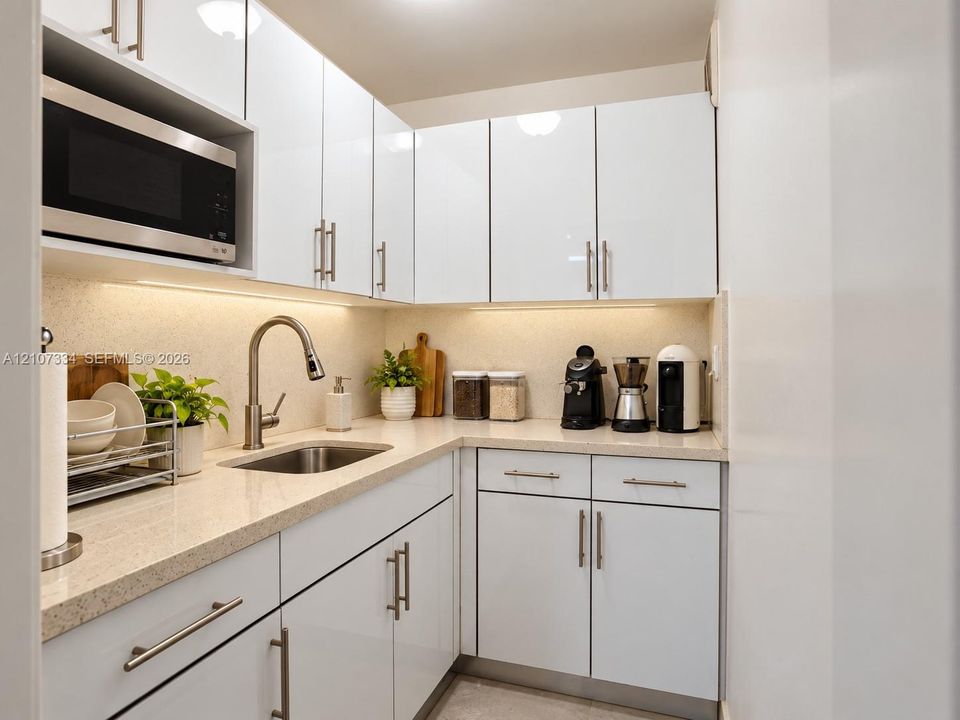 High-gloss white cabinetry, stone-finish countertops, stainless steel undermount sink, brushed nickel pull-down faucet, and built-in microwave