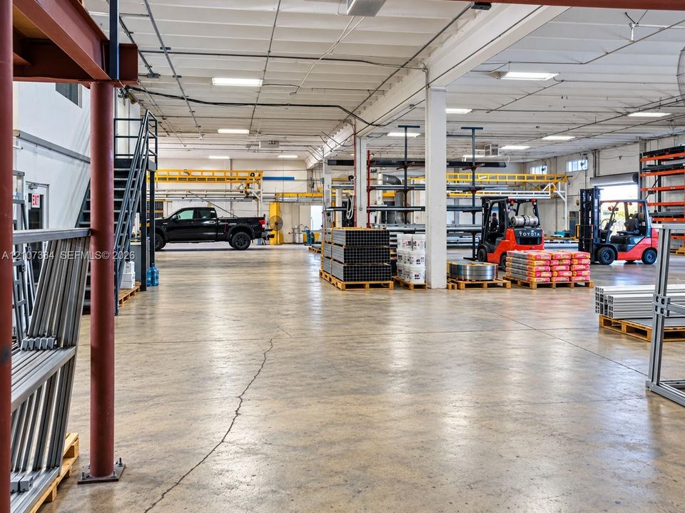 Industrial warehouse space featuring high-clearance ceilings, exposed steel structural beams, polished concrete flooring, and linear overhead lighting