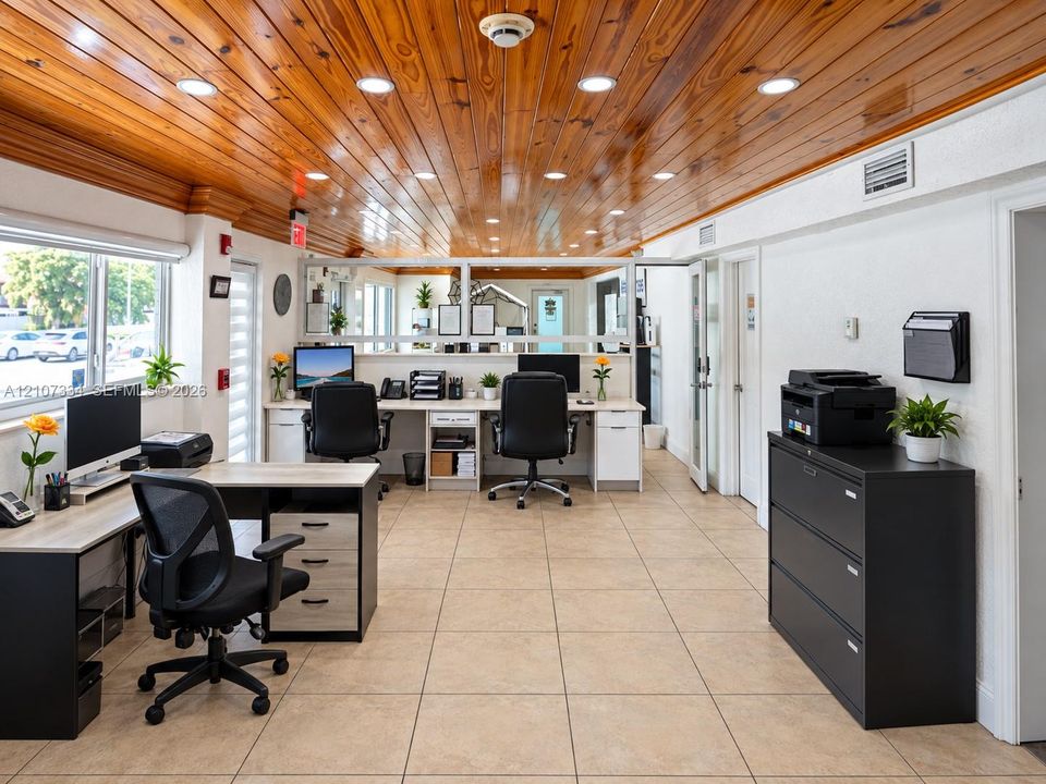 Expansive office interior featuring natural wood-plank ceiling, recessed lighting, large pane windows, and neutral tile flooring