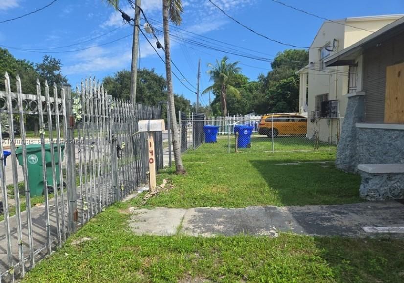 Exterior yard space featuring a metal perimeter fence, concrete walkway, and palm trees