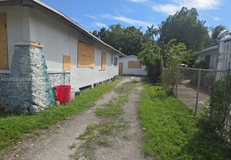 Exterior of a single-story structure with stone-textured masonry siding and a detached secondary structure, featuring an unpaved driveway and metal chain-link fencing
