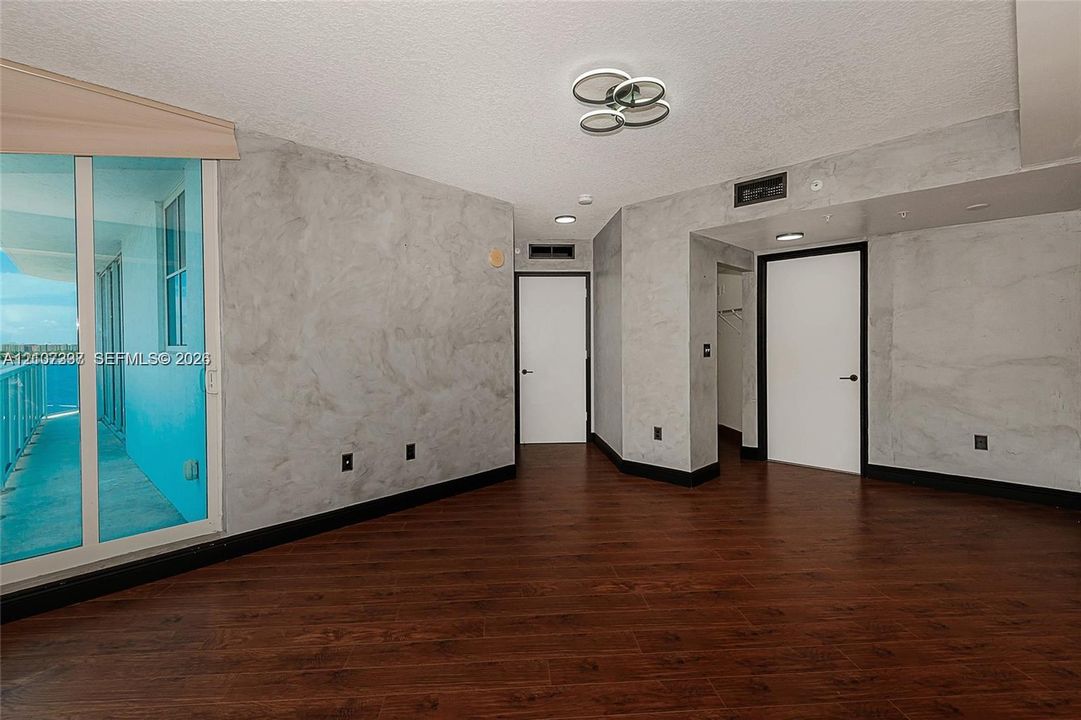 Interior space featuring wood-finish flooring, decorative wall treatment, multi-light flush mount fixture, and sliding glass door access to an exterior balcony