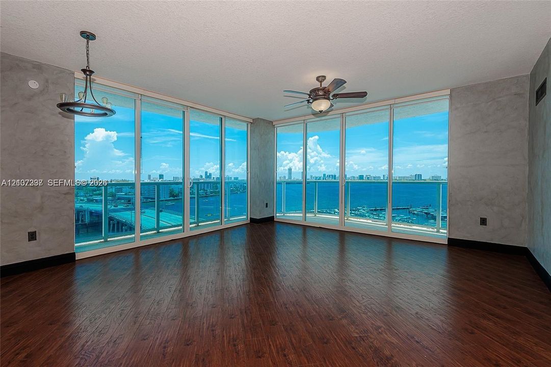 Floor-to-ceiling windows, wood-finish flooring, textured wall treatments, ceiling-mounted light fixture, and integrated ceiling fan