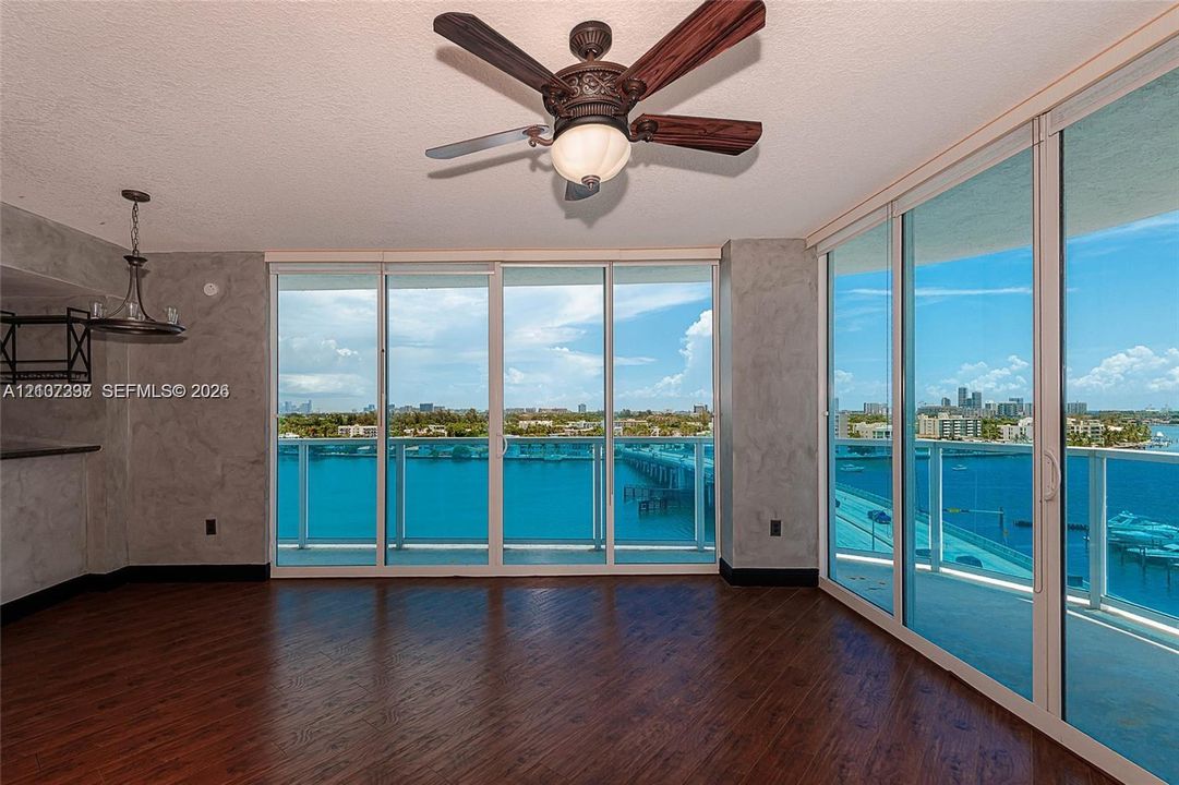 Floor-to-ceiling sliding glass walls, wood-finish flooring, ceiling fan with integrated light fixture, and textured gray wall finishes