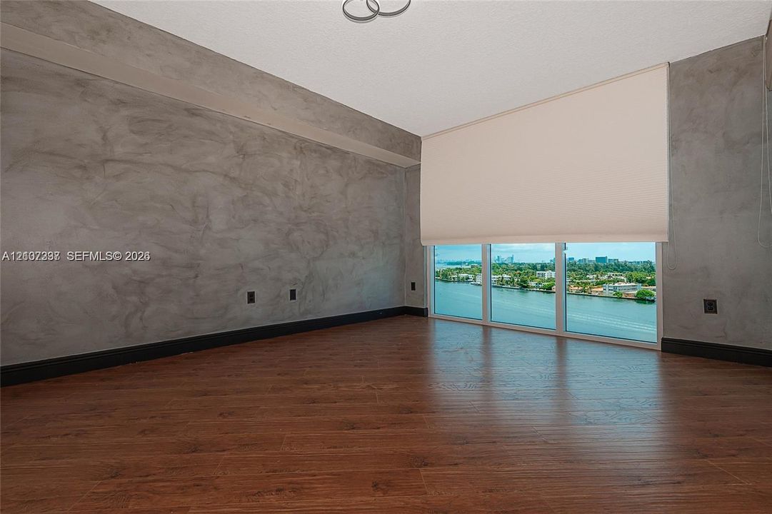 Room featuring textured gray accent walls, wood-finish flooring, and floor-to-ceiling windows with water scenery