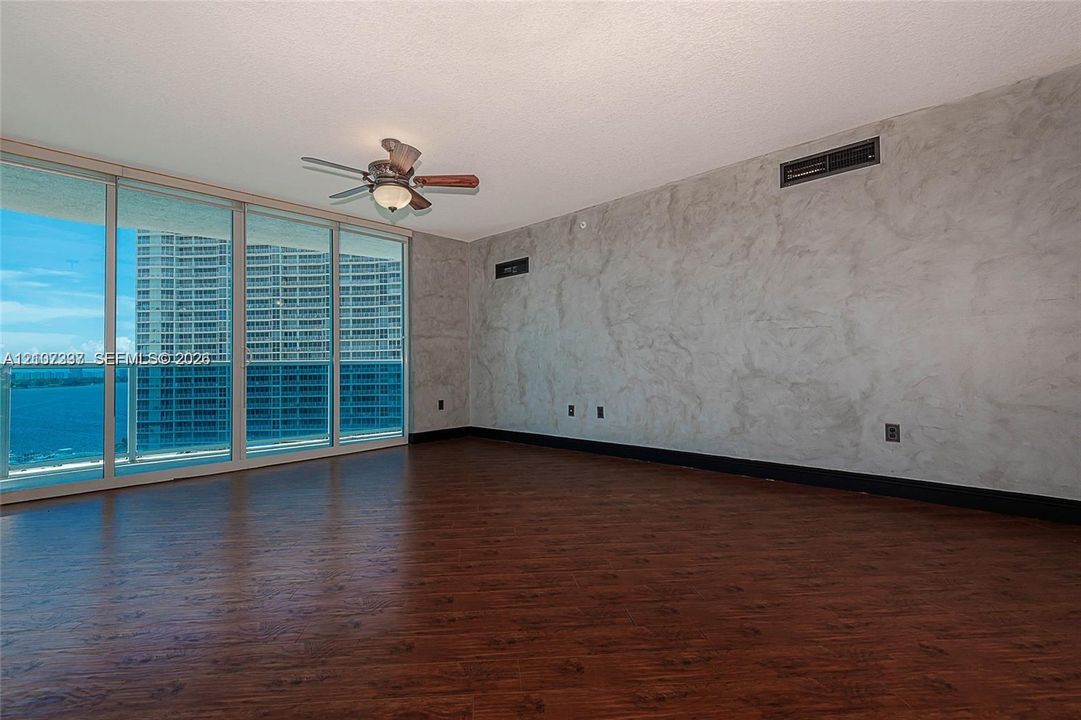 Floor-to-ceiling sliding glass doors, dark wood-finish flooring, decorative plaster wall finish, and a ceiling-mounted lighting fixture with an integrated fan