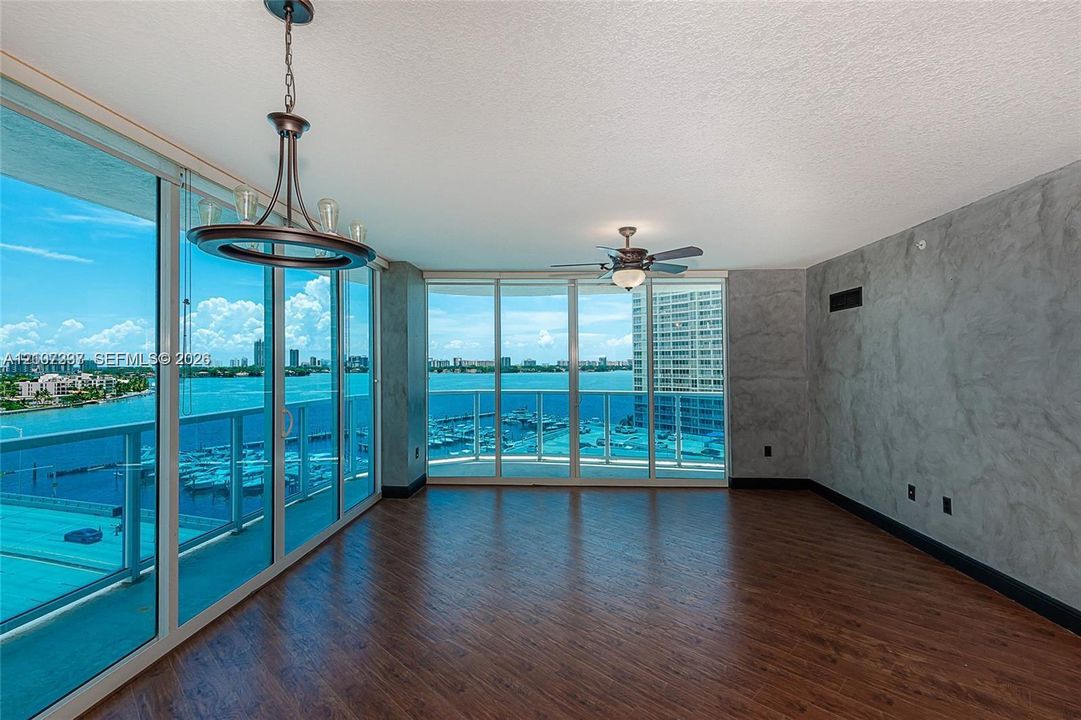 Floor-to-ceiling glass windows, wood-finish flooring, custom textured wall finish, integrated ceiling fan, and multi-light chandelier