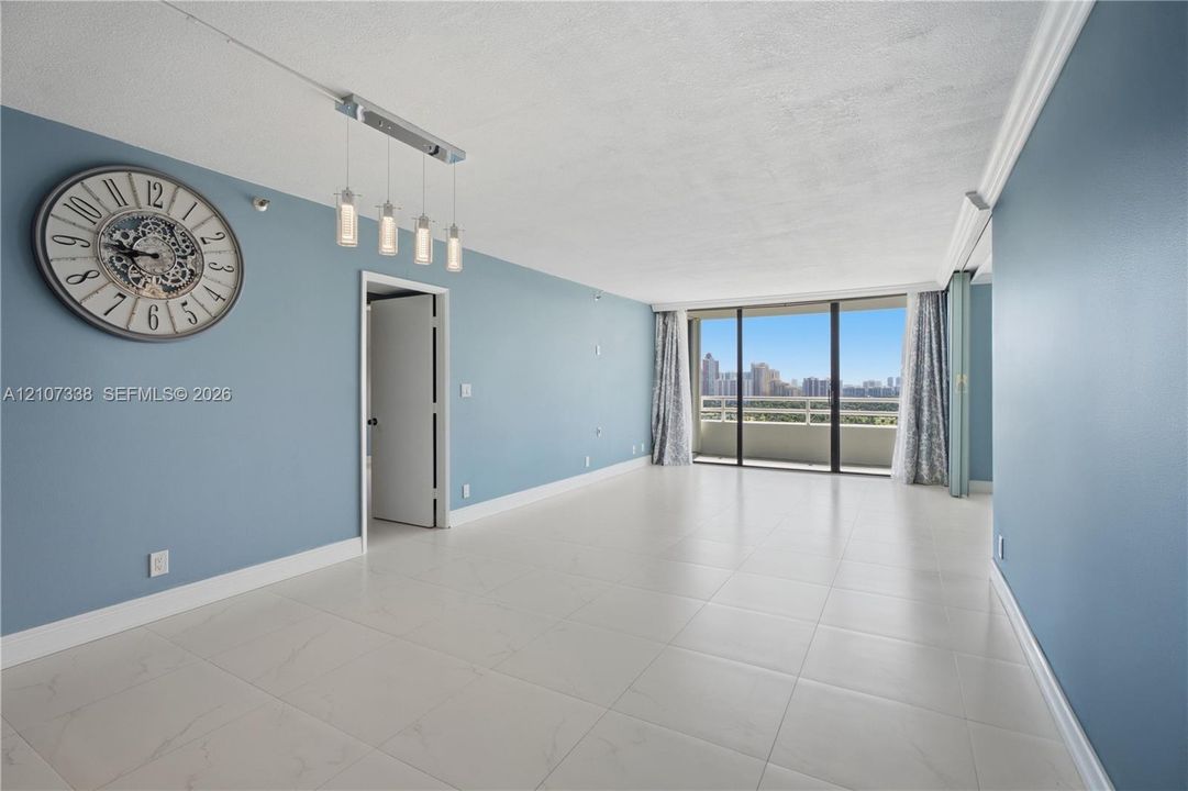 Open-concept living space featuring large-format tile flooring, floor-to-ceiling glass sliding doors, private balcony, and multi-light linear pendant fixture