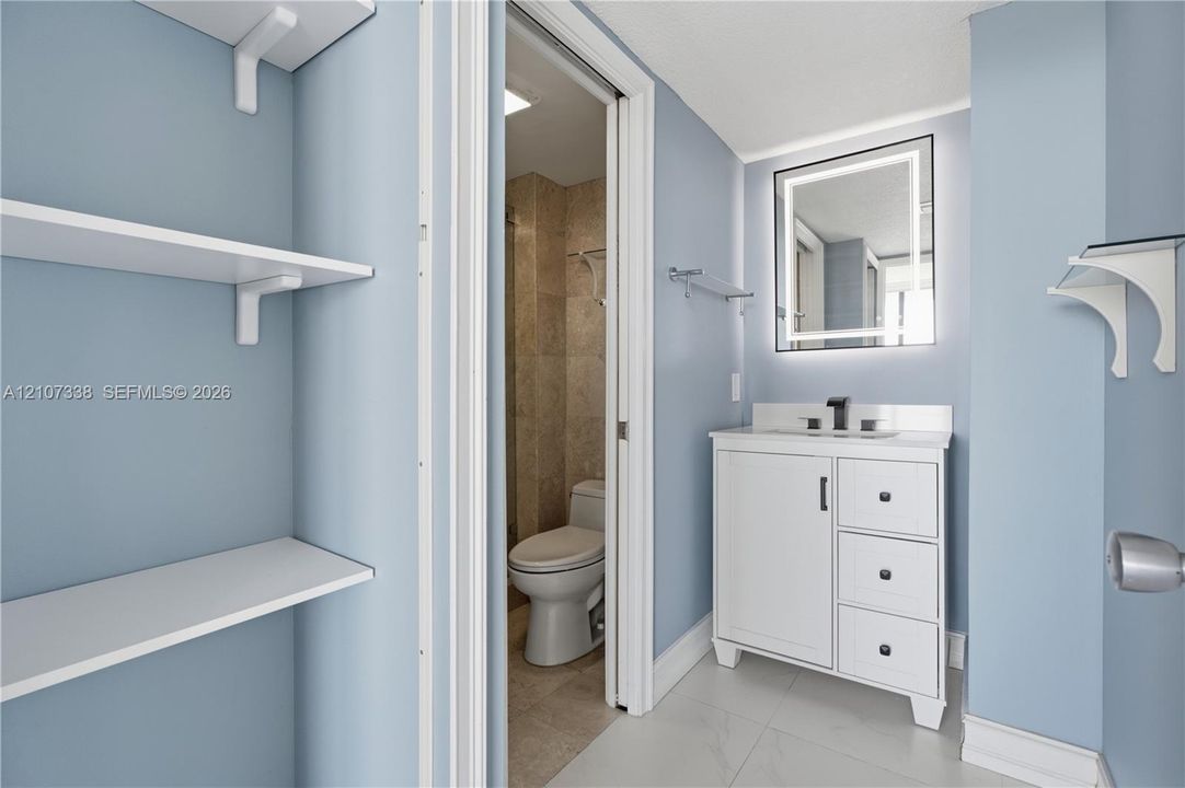 Vanity featuring a white cabinet with integrated drawers, stone countertop, matte black faucet, and an illuminated rectangular mirror
