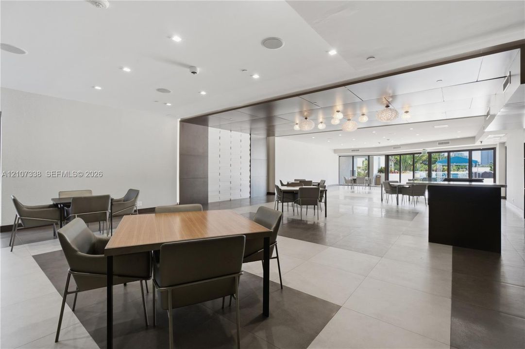 Spacious interior featuring large-format tile flooring, a dark-toned drop ceiling with integrated recessed lighting, decorative globe pendant lights, and floor-to-ceiling glass panel doors