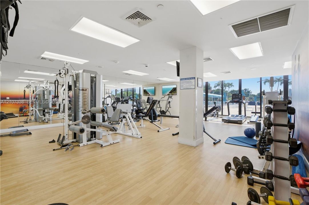 Fitness center featuring wood-finish flooring, full-length wall mirrors, recessed lighting, and floor-to-ceiling windows