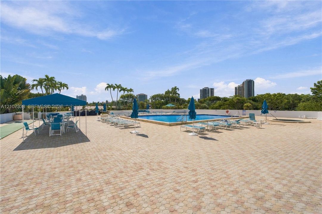 Rooftop pool deck with stone paver surfacing, rectangular swimming pool, integrated spa, and permanent metal-frame canopy structure