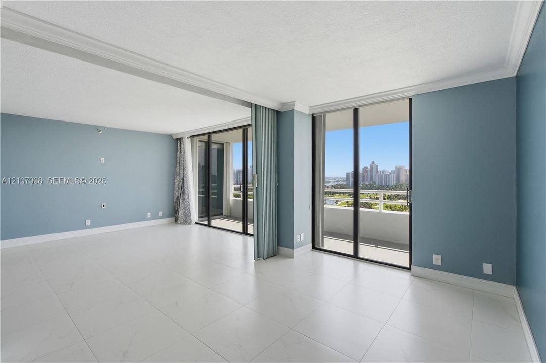 Large-format tile flooring, crown molding, and floor-to-ceiling sliding glass doors opening to a balcony with cityscape scenery