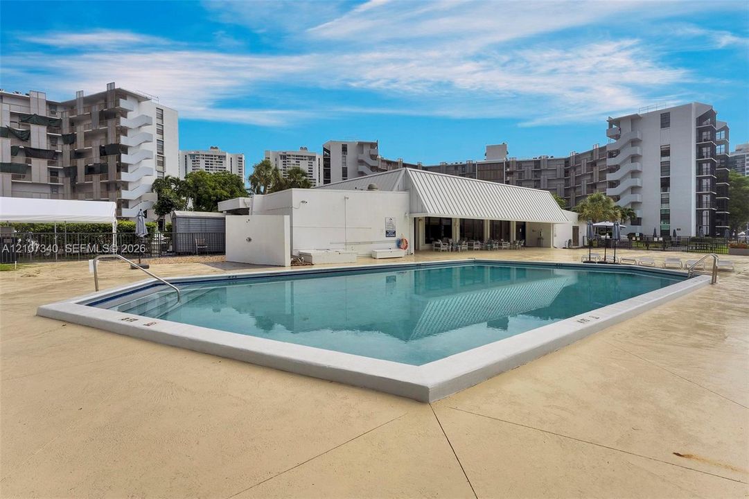 Multi-story residential building exterior featuring a covered entryway, paved surface parking, and curated landscaping