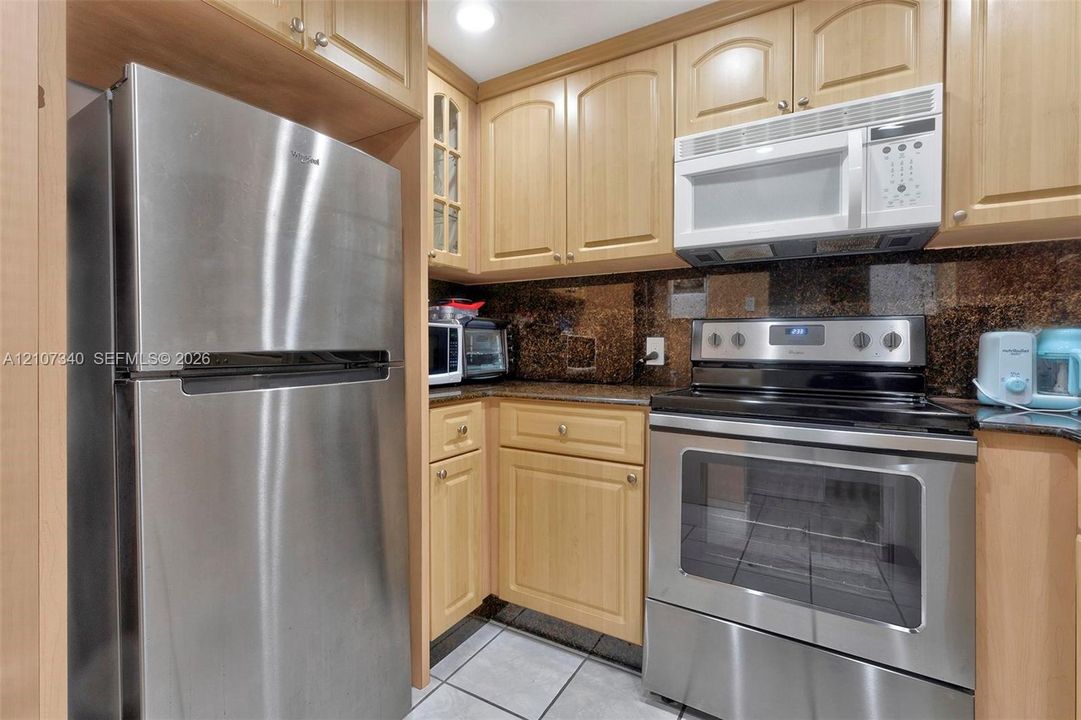 Kitchen featuring light wood cabinetry, stone countertops, stainless steel refrigerator, integrated microwave, and stainless steel electric range