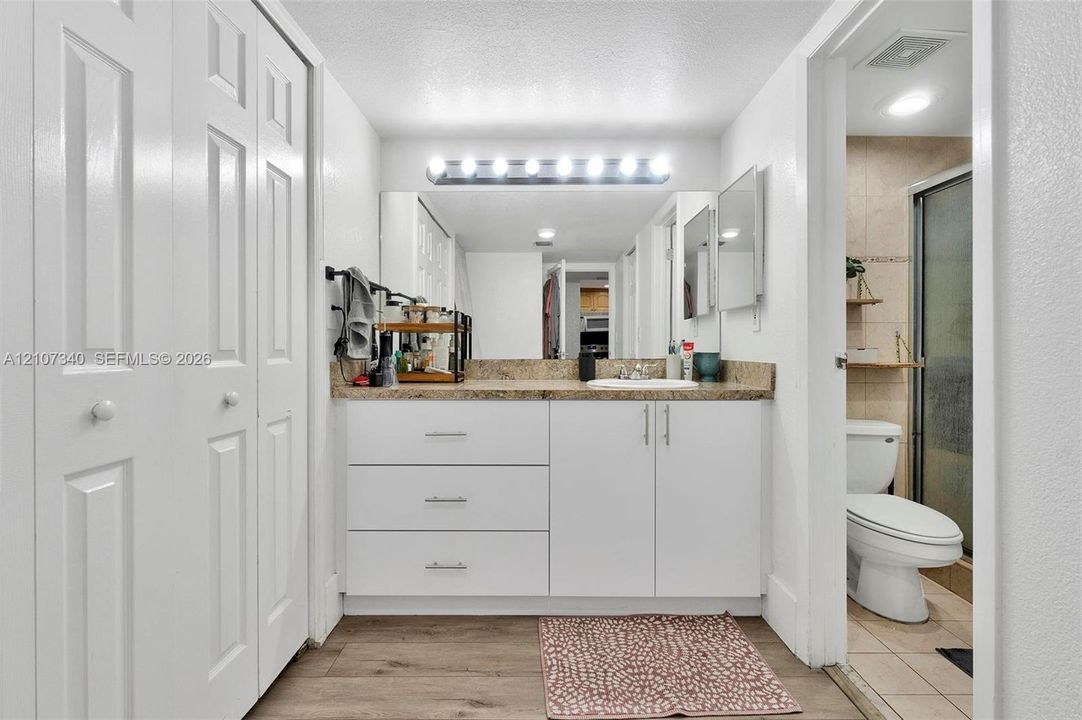 Bathroom featuring white cabinetry, stone-finish countertop with an integrated basin, full-width wall mirror, multi-bulb vanity lighting, and wood-finish flooring