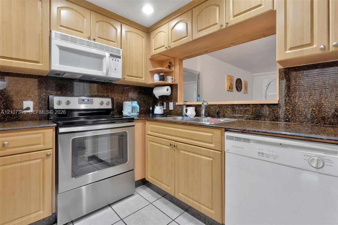 Kitchen featuring natural wood cabinetry, stone-surface countertops, stainless steel electric range, over-the-range microwave, and tile flooring