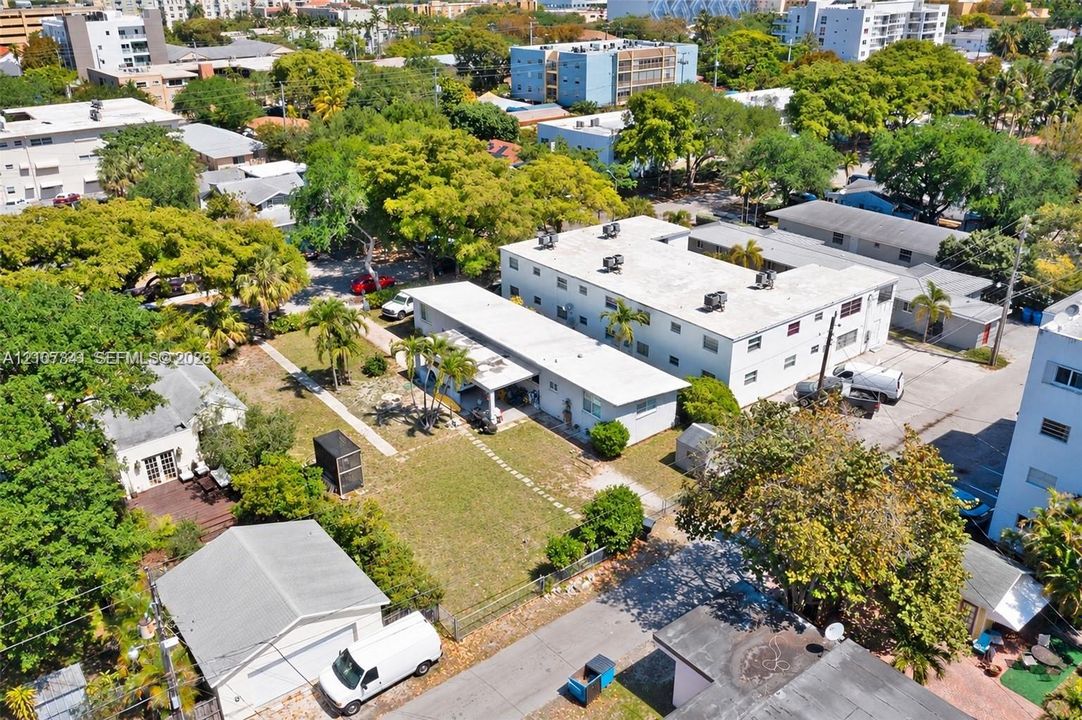 Aerial perspective of a multi-unit residential property featuring a low-rise building, detached garage structure, paved parking area, and mature landscaping