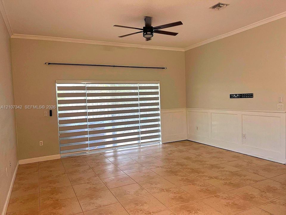 Spacious interior featuring large-format ceramic tile flooring, beadboard wainscoting, and a central ceiling fan