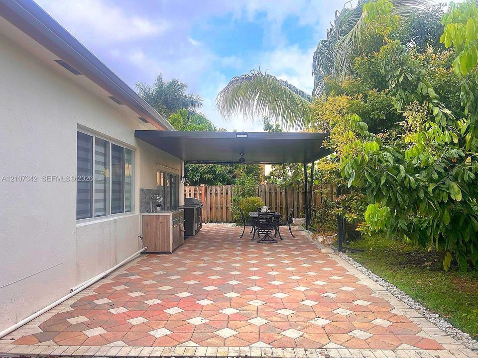 Covered patio featuring patterned stone pavers, a built-in outdoor kitchen station, and perimeter wood fencing