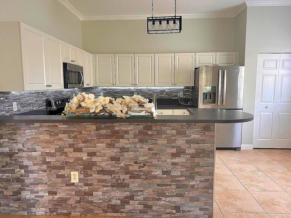 Kitchen featuring off-white cabinetry, stacked stone backsplash, stone-veneer breakfast bar, stainless steel appliances, and cage-style pendant lighting