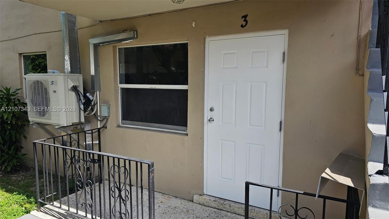 Exterior entry featuring a six-panel door, single-hung window, wall-mounted HVAC unit, and decorative metal railing