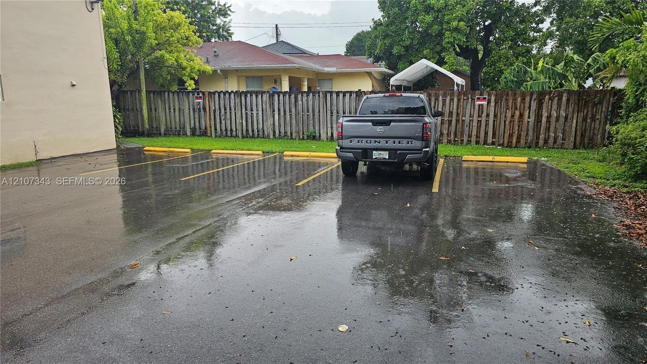 Paved asphalt parking area featuring designated lined spaces, yellow wheel stops, and a wood privacy fence