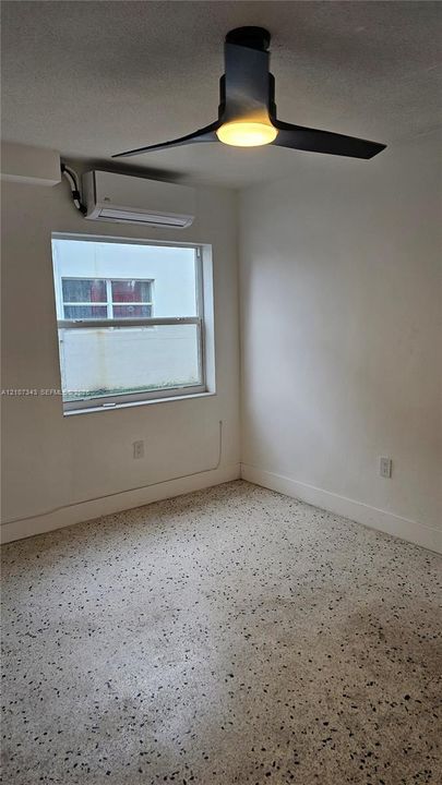 Room featuring terrazzo flooring, wall-mounted ductless climate control unit, and a modern matte black ceiling fan with an integrated light fixture
