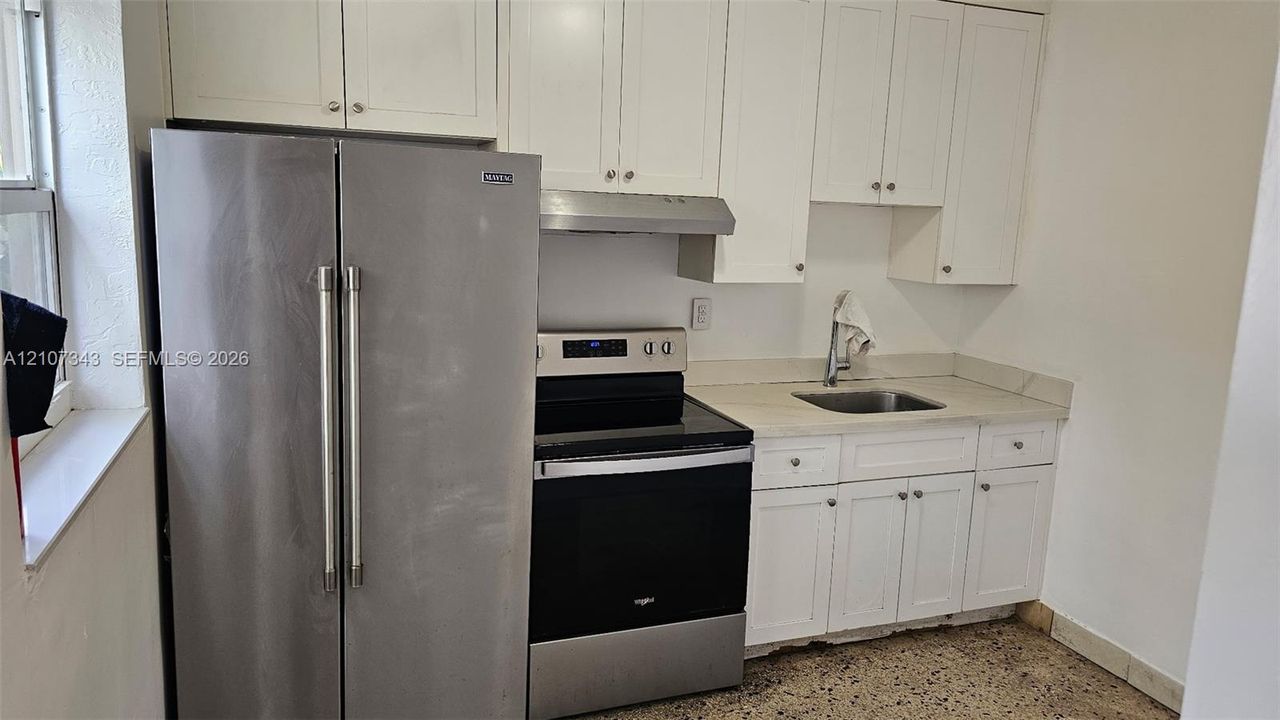 Kitchen featuring white shaker-style cabinetry, stainless steel side-by-side refrigerator, stainless steel electric range, undermount stainless steel sink, and terrazzo flooring