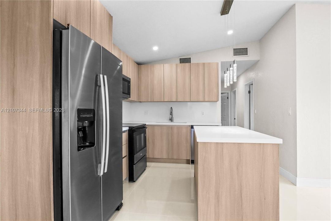 Kitchen featuring wood-finish cabinetry, a center island with a quartz countertop, stainless steel appliances, and pendant lighting