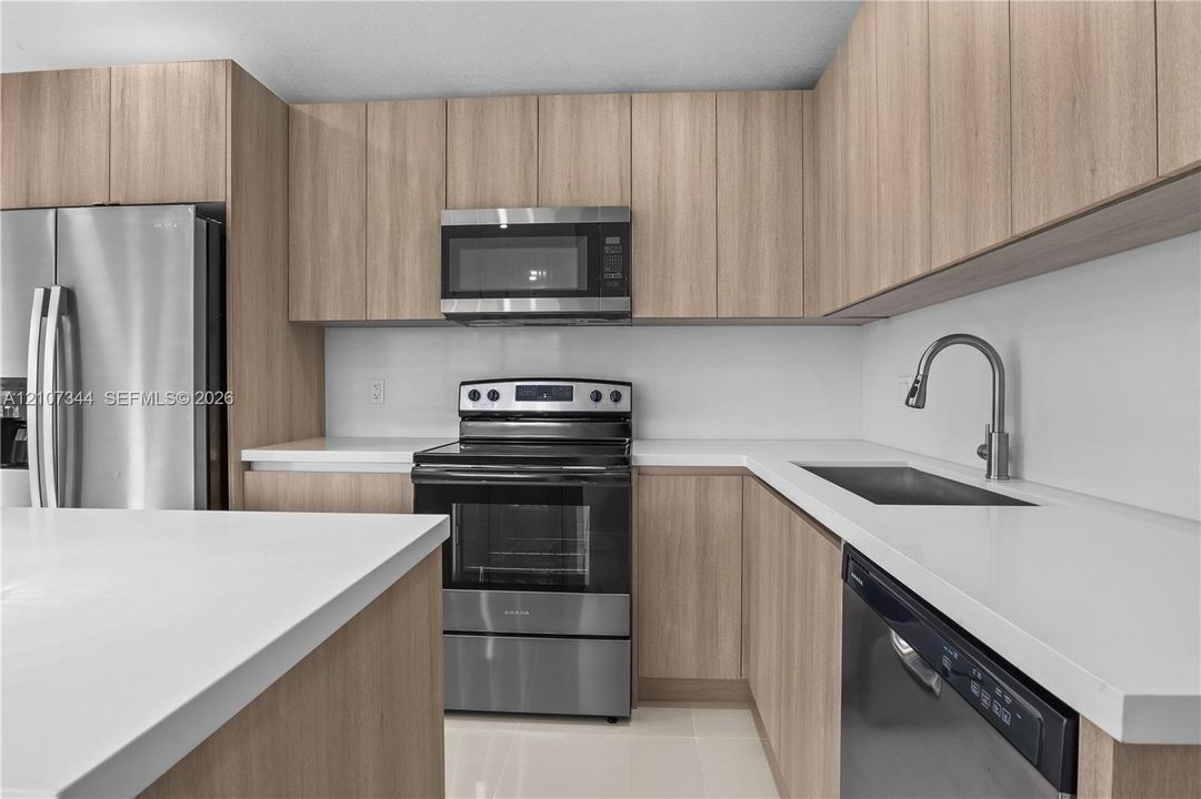 Kitchen featuring wood-finish flat-panel cabinetry, white solid-surface countertops, stainless steel appliances, and a high-arch gooseneck faucet