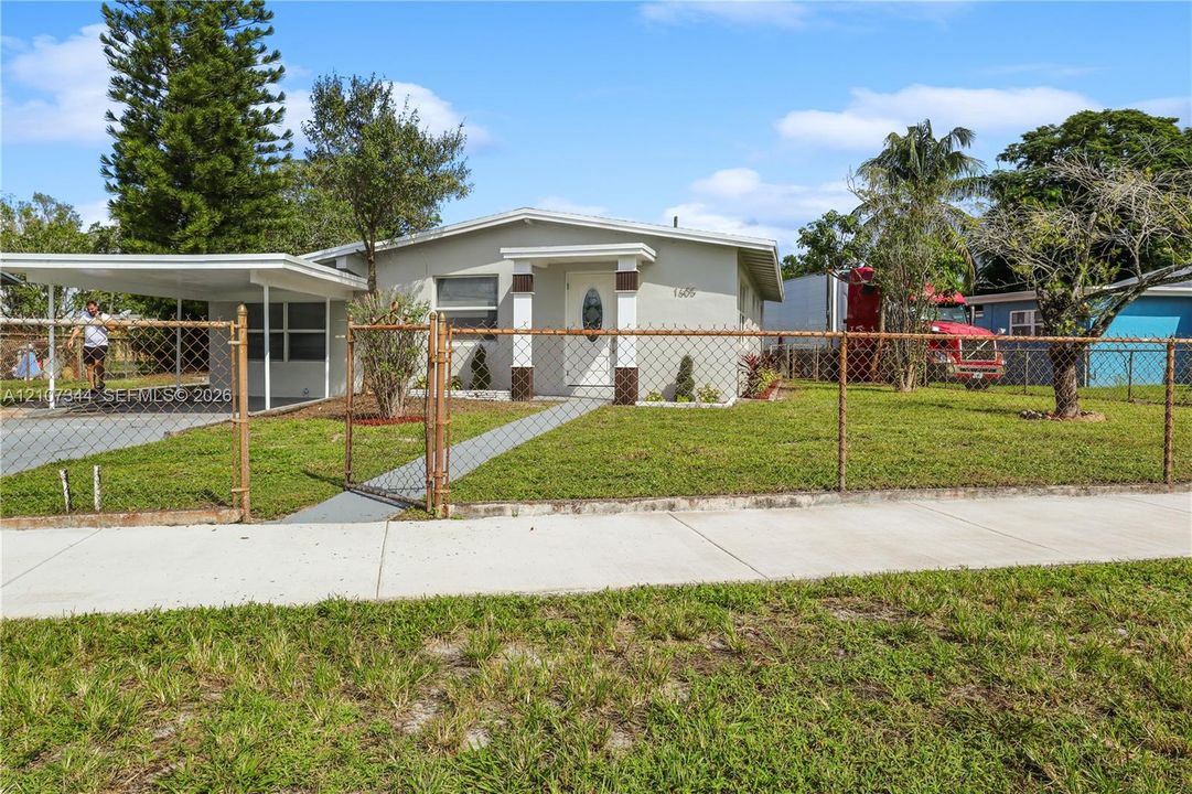 Single-story residence featuring a covered carport, concrete walkway, and chain-link perimeter fencing