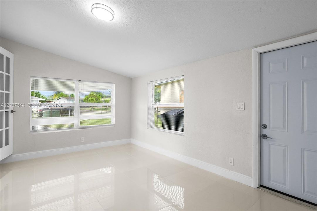 Interior space featuring large-format tile flooring, neutral wall paint, dual windows, a flush-mount circular ceiling light, and a paneled entry door