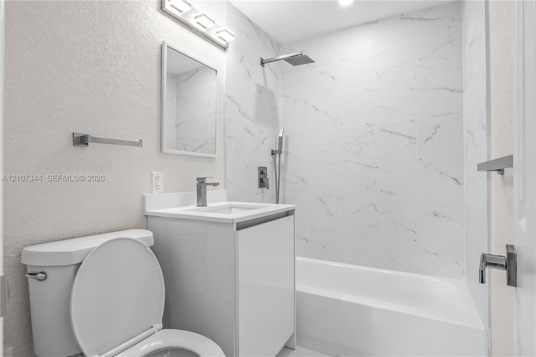 Bathroom featuring a full-height tile surround with a marble-finish pattern, a sleek white vanity with a rectangular sink, wall-mounted modern faucet hardware, and a rainfall shower head