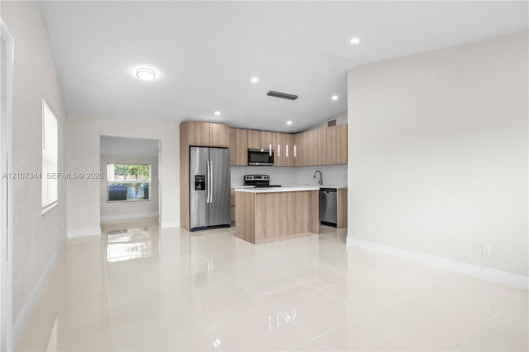 Kitchen featuring light-tone wood cabinetry, a center island with a stone-surface countertop, stainless steel appliances, and large-format porcelain tile flooring