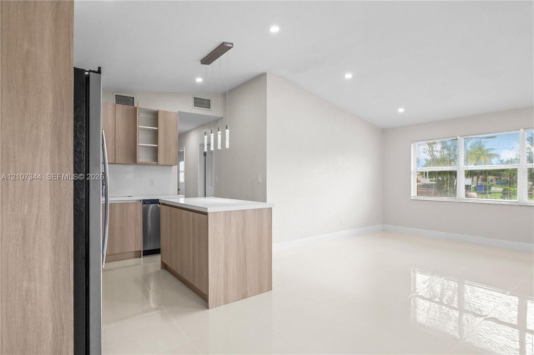 Open-concept kitchen featuring light wood-finish cabinetry, a central island with a white countertop, recessed lighting, and polished tile flooring