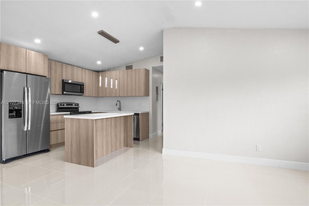 Kitchen featuring wood-finish flat-panel cabinetry, stainless steel appliances, a center island with solid-surface countertop, recessed lighting, and tile flooring