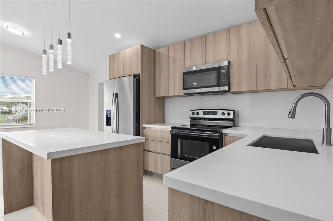 Kitchen featuring flat-panel wood-finish cabinetry, white solid-surface countertops, stainless steel appliances, a center island, and pendant lighting