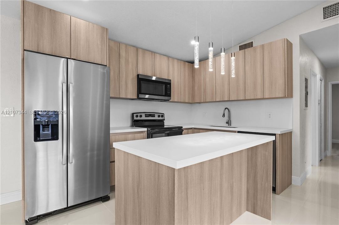 Kitchen featuring wood-finish cabinetry, a central island with a solid surface countertop, stainless steel appliances, and pendant lighting