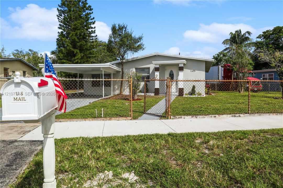 Single-story exterior featuring a covered carport, concrete walkway, and chain-link perimeter fencing