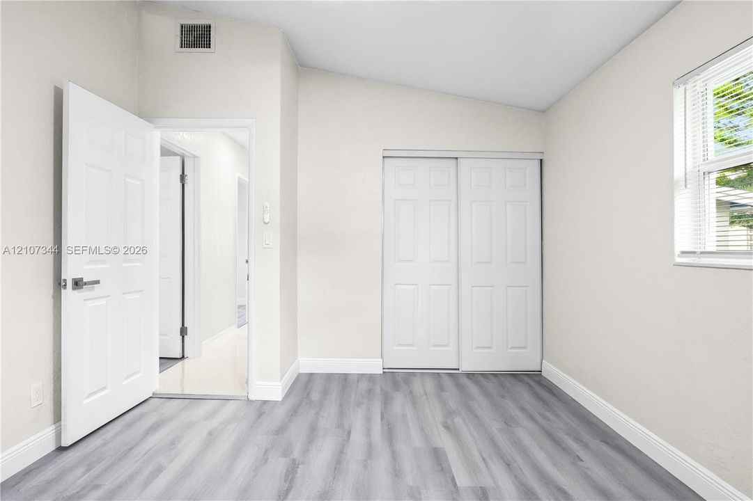 Room featuring wood-finish flooring, a vaulted ceiling, sliding-panel closet doors, and a single-hung window with horizontal blinds