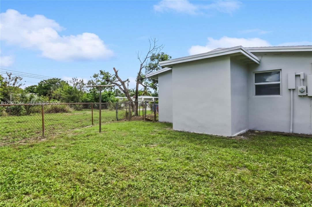 Exterior featuring a light-toned stucco finish, single-hung window, chain-link perimeter fencing, and open greenspace