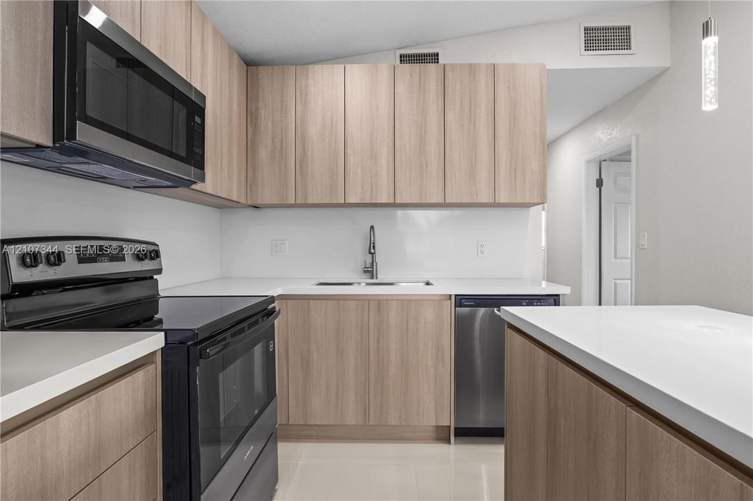 Kitchen featuring light wood-finish cabinetry, solid surface countertops, a white backsplash, and stainless steel appliances, including an integrated microwave and dishwasher