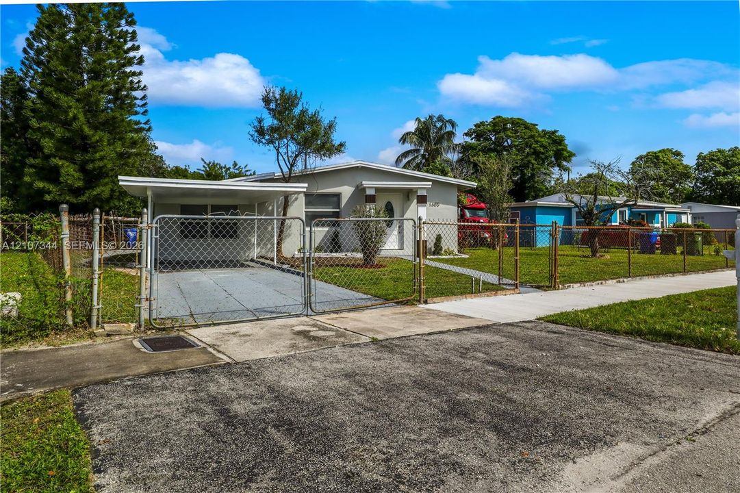 Single-story exterior featuring a painted stucco facade, attached carport, chain-link perimeter fencing, and concrete driveway