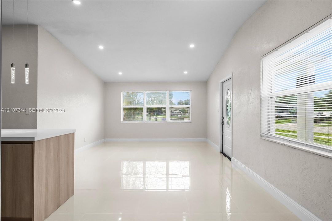 Open-concept room featuring light-toned tile flooring, recessed ceiling lighting, a wood-finish peninsula with a solid-surface countertop, and dual pendant light fixtures