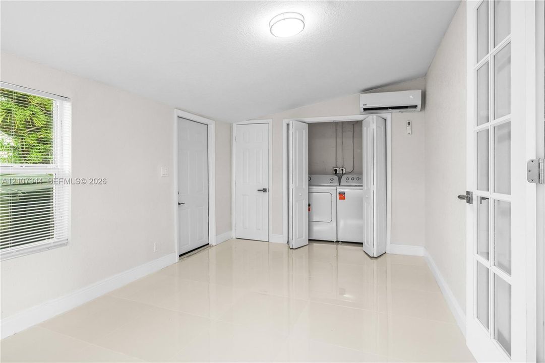 Large-format tile flooring, wall-mounted climate control unit, bi-fold laundry closet, and glass-paneled interior door