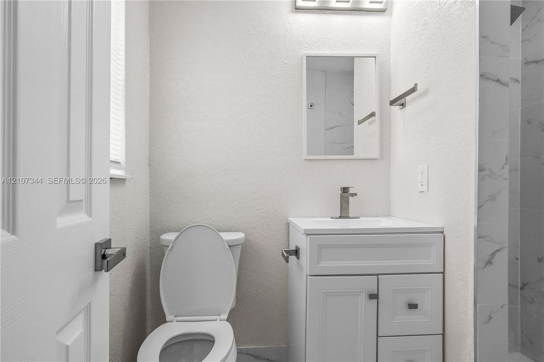 White vanity with integrated basin, single-handle faucet, rectangular wall mirror, and walk-in shower featuring tiled surround